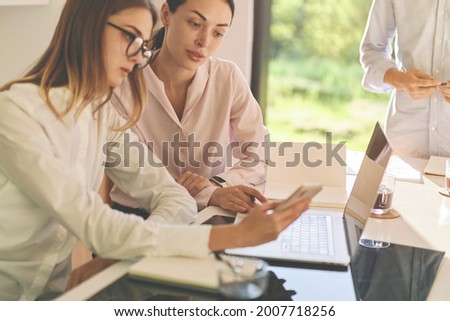 Two focused women at working process. Two beautiful businesswomen working together with laptop at modern office