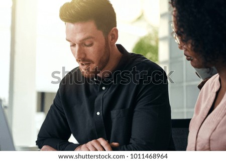 Two focused young work collegues talking business together while sitting at a table in a modern office