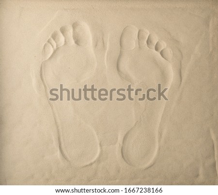 Two footprints on light beige sea sand texture, footstep pattern. Sandy beach textured background with two barefoot prints top view