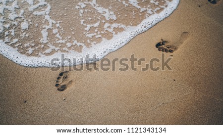 Two footprints on sand at the beach with waves and foam