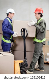 Two Foremen Lifting Cardboard Box At Warehouse