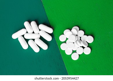 two forms of medicinal tablets; a handful of oval long pills and a bunch of round pressed pills on a modern designer background of two shades of green