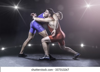 Two freestyle wrestlers in red and blue uniform wrestling against the lights on background