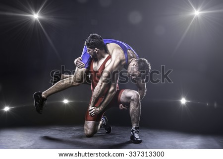 Two freestyle wrestlers in red and blue uniform wrestling against the lights on background