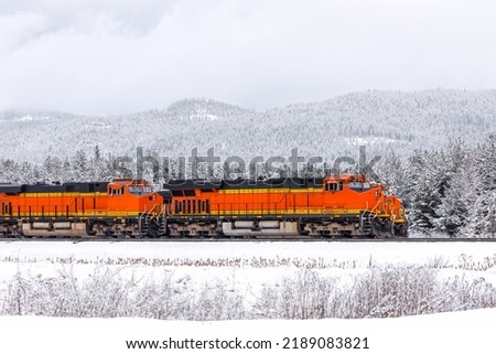 two freight trains, with three locomotives visible, pulling cargo through mountainous region close to Whitefish, Montana in winter