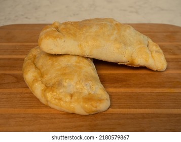 Two fresh baked beef and potato pasties on a wooden cutting board.