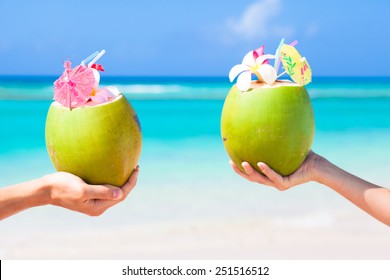Two fresh coconut cocktails with umbrellas in hands