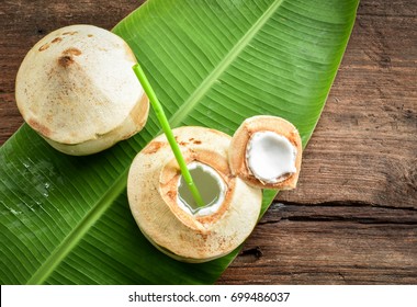 Two fresh coconut fruits ready to serve as beverage. Young coconut fruit cut open to drink sweet  juice and eat. Flat lay on green banana leaf and wood background.
