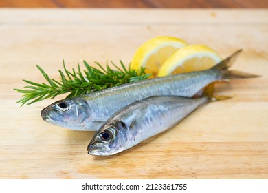 Two Fresh Sardine Fish Decorated With Lemon And Rosemary On A Wooden Pad