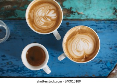 two fresh tasty cappuccino coffee cups with latte art on it and one espresso cup with beautiful tiger crema on the coffee table - Powered by Shutterstock