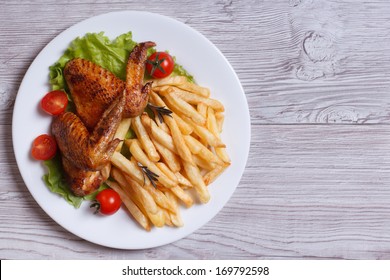 Two Fried Chicken Wings, French Fries, Tomato And Lettuce On A Plate. Top View