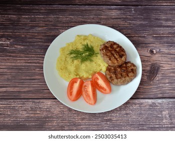 Two fried cutlets and mashed potatoes with tomato slices on a wooden table. Top view, flat lay.