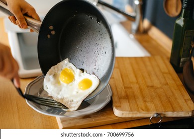 Two fried eggs in a pan with olive oil. Girl's hand holding a frying pan with scrambled eggs.