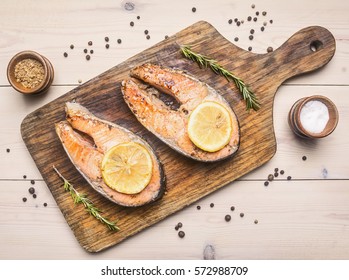 two fried fresh salmon steak with unground pepper, spices and lemon on a cutting board top view