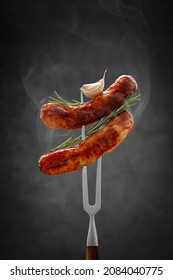 Two Fried Hot Thinking Sausages On A Meat Fork With Raspberry And Garlic. Grilled Sausage, Bbq Concept