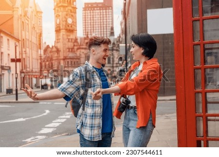 two friend, couple using a camera,   taking selfie against a red phonebox, watching photos on camera, having a fun  in the city of England.Travel Lifestyle concept