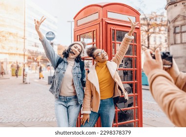 dos amigas, novia y mujeres que usan un teléfono móvil, cámara y toman selfie contra una caja de teléfonos roja en la ciudad de Inglaterra.concepto de estilo de vida de viaje