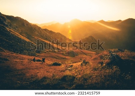 Two friend hikers in distance trekking left side on trail outdoors on beautiful sunset in autumn together. Active people on trek in caucasus mountains