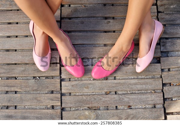 two\
friend women sitting cross legged wearing pink\
flats