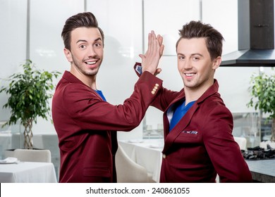 Two friendly brothers twins in red jackets and blue sweater together having fun in the dinner room or the restaurant. Family relationships or friends in business