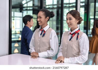 Two friendly female airport ground staffs in airline uniforms standing at airport check in counter, airline workers working at airport , happy airline ground workers smiling at check in desk 