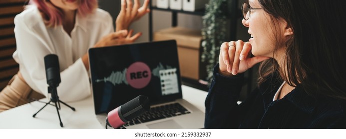 Two friendly women host streaming audio podcast using microphone and laptop at home broadcast studio - Shutterstock ID 2159332937