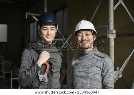 Two friendly workers on site (steeplejacks and outdoor workers with safety belt harnesses) smiling for the camera.