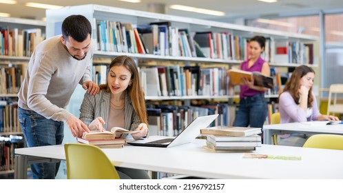 Two Friendly Young Adult Male And Female Students Preparing For Exam Together In University Library, Using Textbooks And Laptop