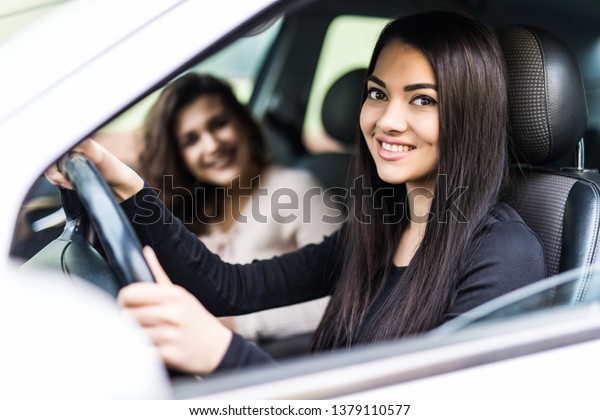 Two friendly young women enjoying a day trip to\
town viewed through the open window of their car grinning happily\
at the camera