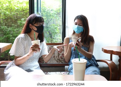 Two Friends Asian Women Wearing Hygienic Mask Sitting And Making Conversation At Wooden Table In Cafe. Social Distance To Prevent From Covid-19.