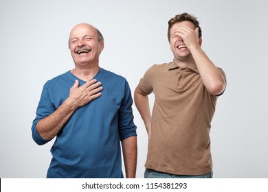 Two Friends In Casual Colorful Wear Standing And Laughing Together. Mature Son And Father Together Chortling . Two Men Having Fun.