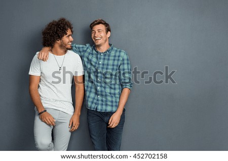 Two friends in casual wear standing and laughing together. Best friends enjoying isolated over grey background. Two men having fun isolated over grey wall with copy space.