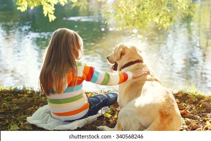 Two Friends, Child With Labrador Retriever Dog Sitting In Sunny Summer Park Near Water