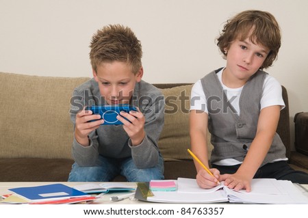 Two friends doing their homework in the livingroom. One of them is gaming, the other one is not ready and is jealous.