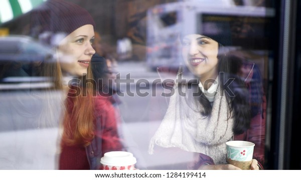 Two friends drink coffee in a cafe with a view to\
the street