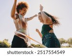 Two friends enjoying fun activities with hula hoops on a sunny day at the park. A joyful outdoor moment.