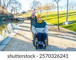 Two friends enjoying a walk in the park, one pushing the other in a wheelchair and pointing at something in the distance