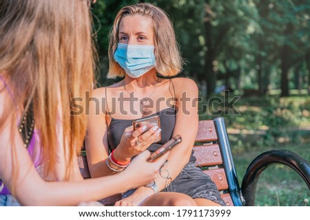 Two friends with face masks talking and using their smartphones