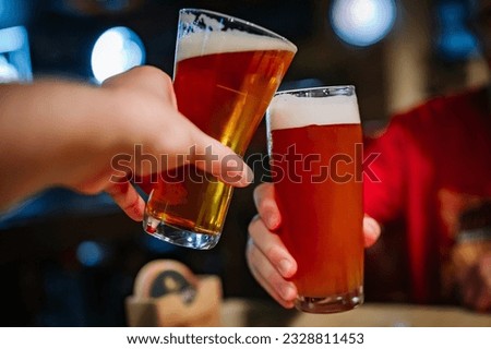 Two friends hands clinking glasses of craft beer at the pub or bar