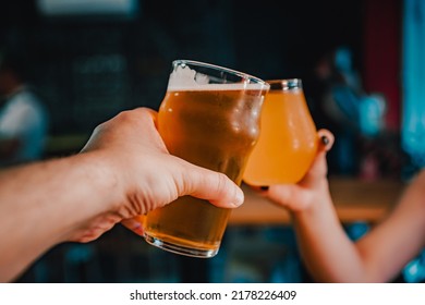Two friends hands toasting with glasses of light beer at the pub or bar.