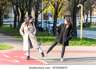 Two friends having a conversation while walking in city  Young women wearing protective face mask and doing the leg handshake greeting 