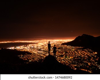 Two Friends Holding Hands Looking Over Cape Town City Lights From On Top Of Lion's Head At Night, South Africa.
