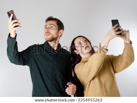 Two friends are holding two smartphones looking at the cell phone screen laughing.
The man looks surprised.
Facial expression of surprised.
Background isolated on white background.