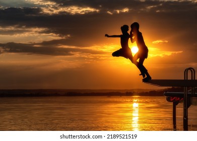 Two Friends Jumping Together In A Lake At Sunset