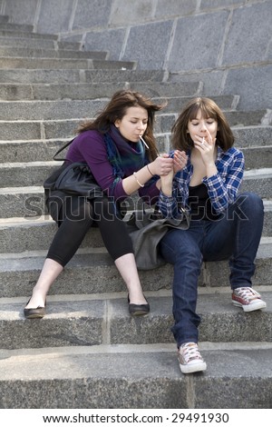 two friends light a cigarette sitting on step