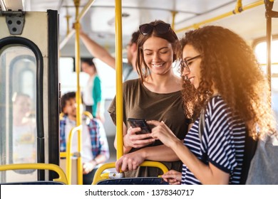 Two friends looking in phone while standing on a bus. - Powered by Shutterstock