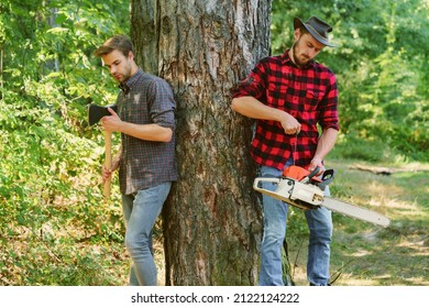 Two friends Lumberjack worker in the forest. Woodcutter with axe and lumberjack with chainsaw. Handsome woodcutter men hipsters in forest.