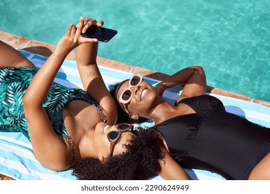 Two friends lying by the pool taking selfies in swimsuits, body positive summer - Powered by Shutterstock