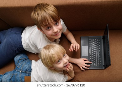 Two Friends Lying On The Couch With Laptop. Generation Alpha Concept.