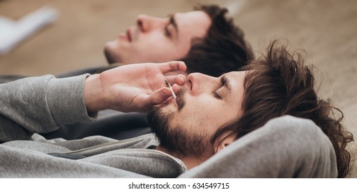 Two Friends Lying On The Ground And Smoke Grass Joint In Abandoned Ghetto Part Of The City